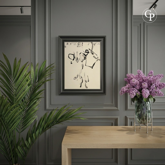 Encre abstraite Élan Lyrique de Hanna Ben-Dov encadrée dans un cadre noir épuré, fixée sur un mur à moulures gris anthracite au-dessus d'une console en bois clair, avec un vase de lilas violets et une plante verte. | Framed abstract ink Lyrical Impulse by Hanna Ben-Dov in a sleek black frame, hanging on a charcoal grey paneled wall above a light wood console table, styled with a vase of purple lilacs and a green plant.