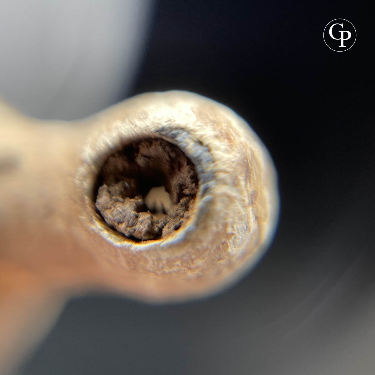 Macro close-up of an ancient Roman lead whistle showing mineralized leather strap remains preserved inside, evidence of functional suspension use | Gros plan macro d’un sifflet antique romain en plomb montrant des restes de lanière de cuir minéralisée conservés à l’intérieur, preuve d’un système de suspension fonctionnel