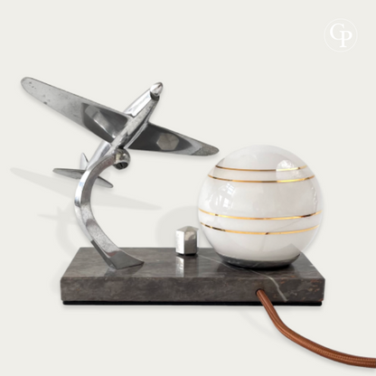Back view of an Art Deco airplane lamp showing the chrome structure, white glass globe with gold stripes, and marble base | Vue arrière d'une lampe avion Art Déco montrant la structure en chrome, le globe en verre blanc à filets dorés et le socle en marbre