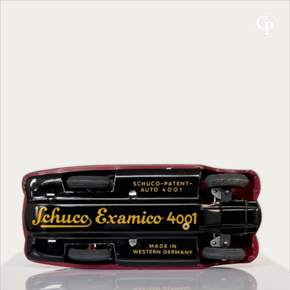 Underside view of the Schuco Examico 4001 toy car chassis, showcasing the original gold lithographed inscriptions 'Schuco Examico 4001' and 'Made in Western Germany' on a light background. | Vue du dessous du châssis de la voiture automate Schuco Examico 4001, mettant en valeur les inscriptions lithographiées dorées d'origine 'Schuco Examico 4001' et 'Made in Western Germany' sur fond clair.