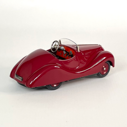Rear left three-quarter view of the deep red Schuco Examico 4001 vintage tinplate roadster, highlighting the detailed orange dashboard, steering wheel, and gear levers on a light background. | Vue arrière gauche de trois-quarts d'une voiture automate Schuco Examico 4001 couleur bordeaux, mettant en valeur le tableau de bord orange détaillé, le volant et les leviers de vitesses sur fond clair.