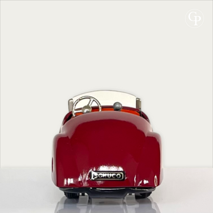 Strict rear view of the deep red Schuco Examico 4001 vintage tinplate roadster, showcasing the Schuco license plate, cockpit interior, and chrome steering wheel on a light background. | Vue de dos de la voiture automate Schuco Examico 4001 de couleur bordeaux, mettant en valeur la plaque d'immatriculation Schuco, l'intérieur de l'habitacle et le volant chromé sur fond clair.